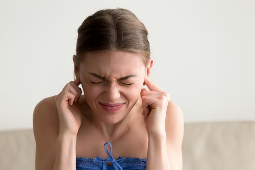 Young annoyed woman sticking fingers in ears, not listening nois